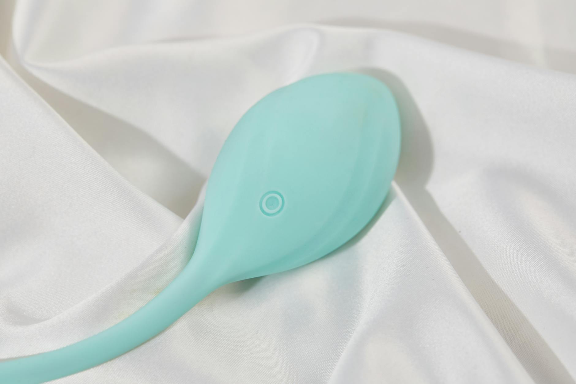 A stylish teal vibrator on smooth white silk fabric representing modern sensuality and pleasure
