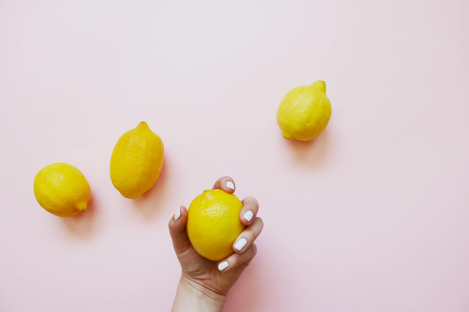 A hand holding a fresh lemon on a soft pink background, symbolizing gentle, gradual healing