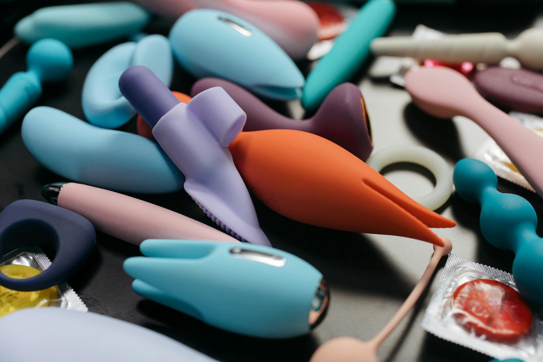 Woman with eyeglasses holding blue and pink silicone vibrators in a contemplative manner.
