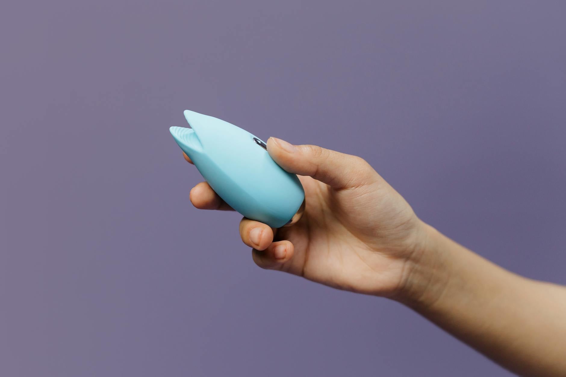 A blue silicone clitoral vibrator held in hand against a purple background, promoting self-love and reclaiming pleasure