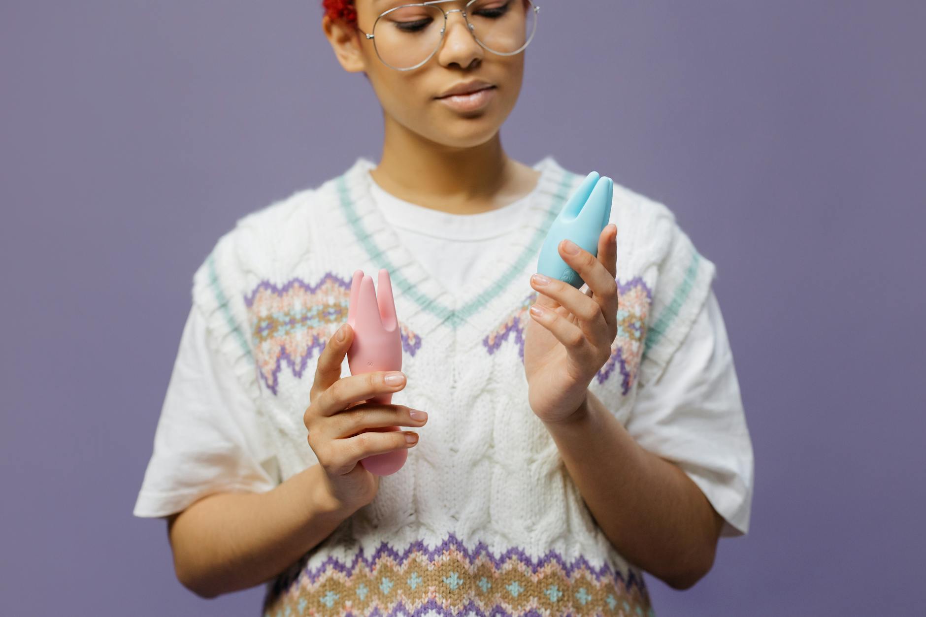 Close-up of a woman holding a pink vibrator, with art books in the background, emphasizing intimate and personal themes.