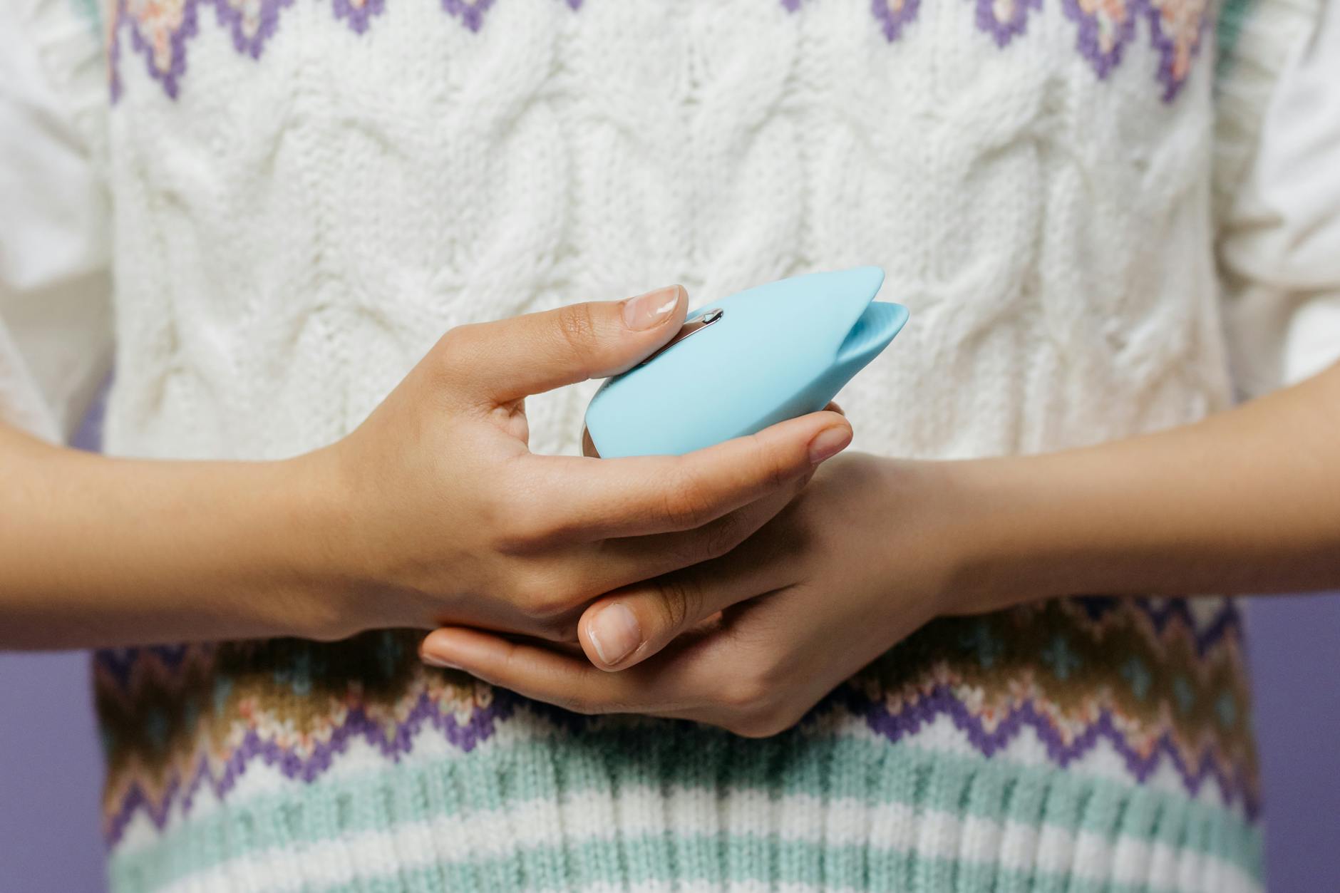 Close-up of hands holding a blue lemon vibrator against a knitted sweater