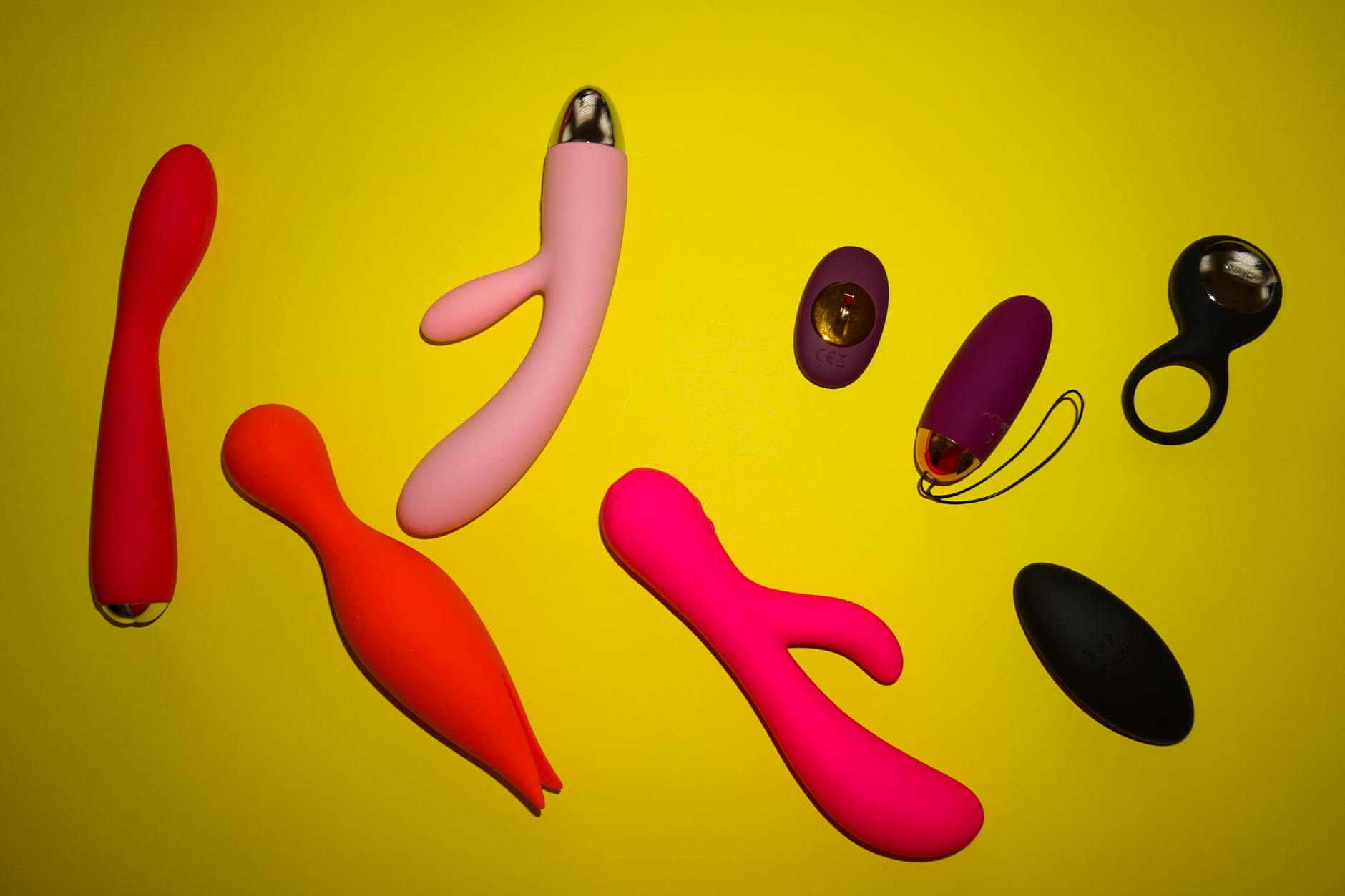 Colorful vibrators and intimate wellness tools arranged on bright yellow surface