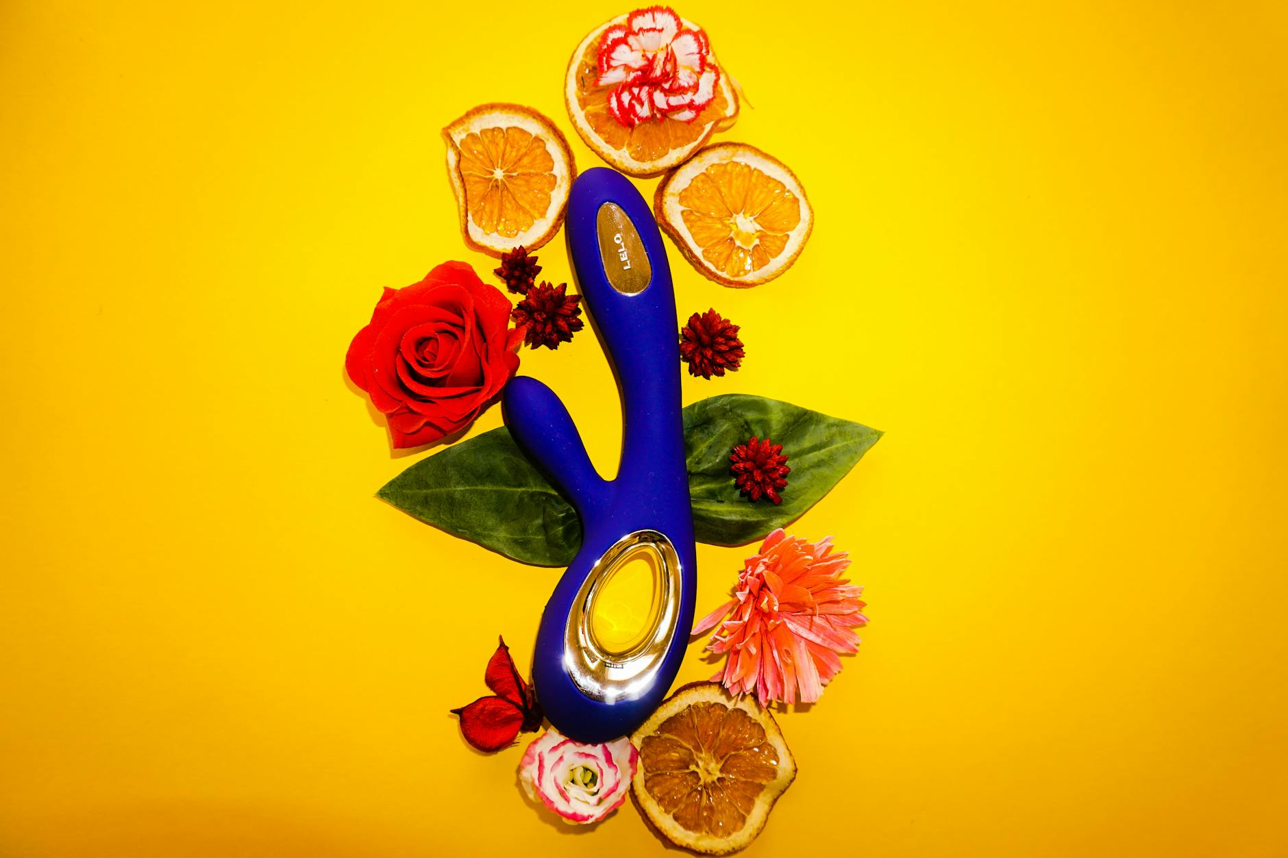 Lemon vibrator surrounded by flowers and fruit on yellow background