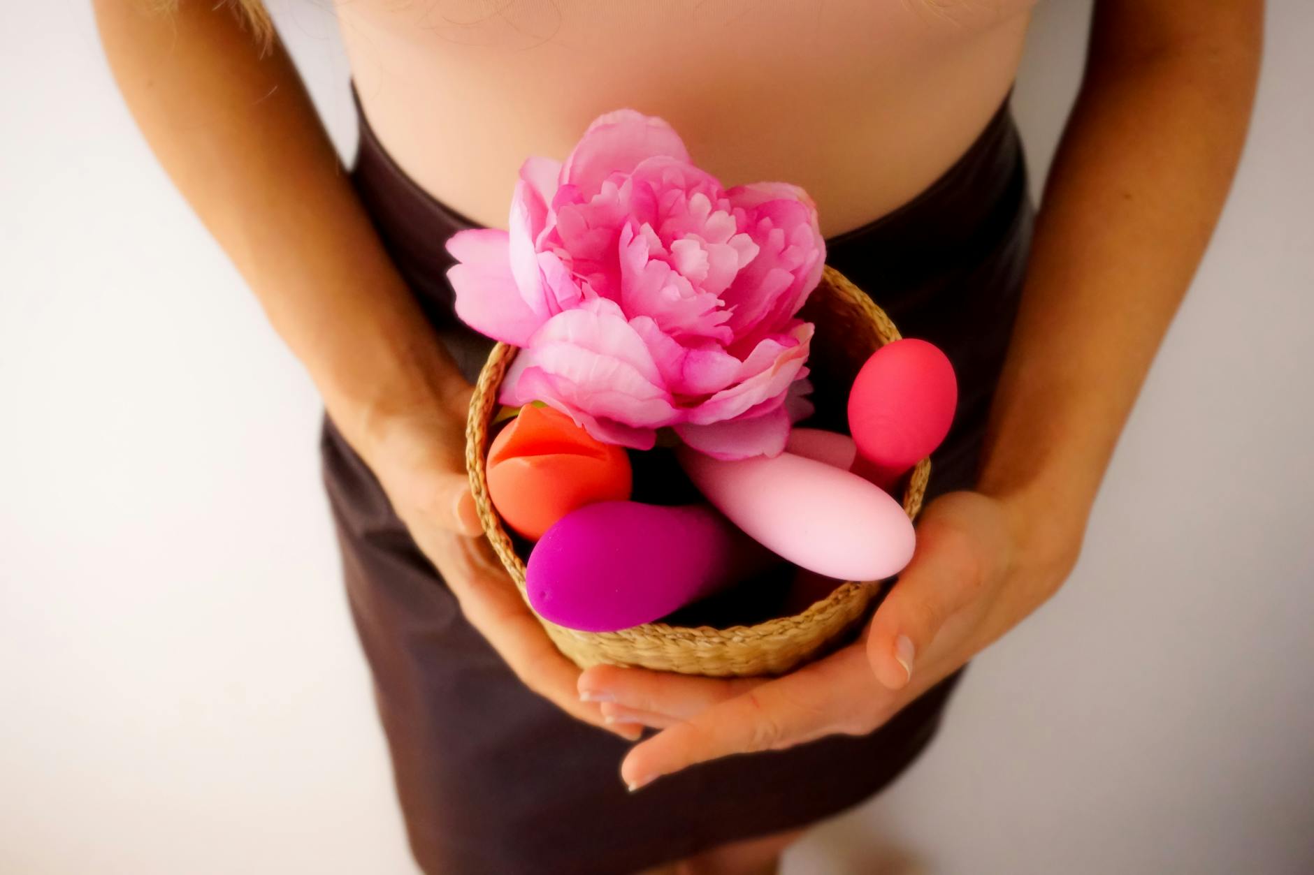 A basket containing colorful vibrators and a pink flower against a soft background